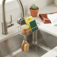 A secure sink caddy organiser attached to a curved kitchen sink edge, holding sponges and cleaning brushes in a tidy kitchen.